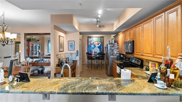 kitchen featuring appliances with stainless steel finishes, a chandelier, kitchen peninsula, and light stone countertops