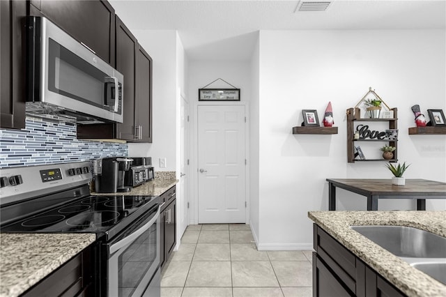 kitchen with decorative backsplash, appliances with stainless steel finishes, dark brown cabinets, light tile patterned flooring, and light stone counters