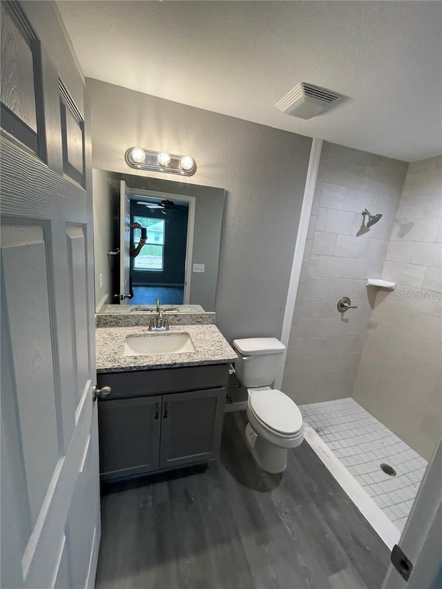 bathroom with a tile shower, vanity, wood-type flooring, and toilet