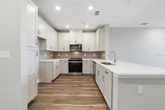 kitchen with appliances with stainless steel finishes, kitchen peninsula, wood-type flooring, sink, and tasteful backsplash