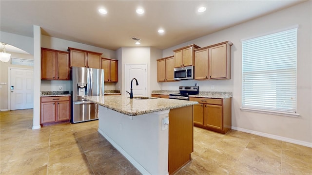 kitchen with a kitchen bar, a center island with sink, appliances with stainless steel finishes, light stone countertops, and sink