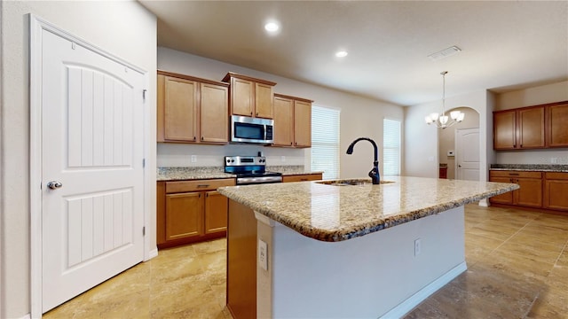 kitchen with an island with sink, appliances with stainless steel finishes, decorative light fixtures, light stone counters, and sink