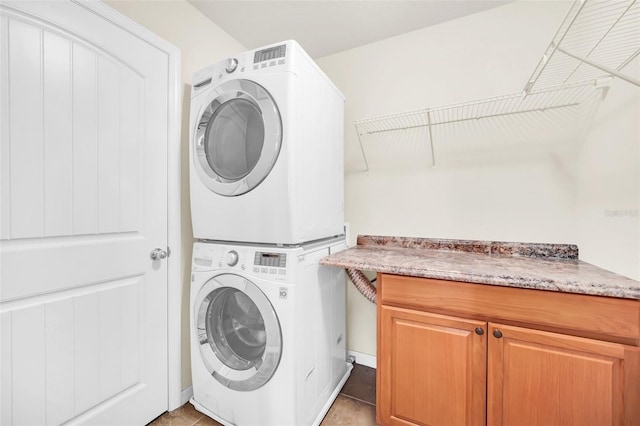 laundry room featuring stacked washer / dryer, light tile patterned flooring, and cabinets