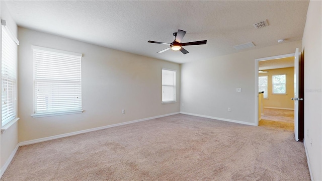 carpeted empty room with ceiling fan, a wealth of natural light, and a textured ceiling