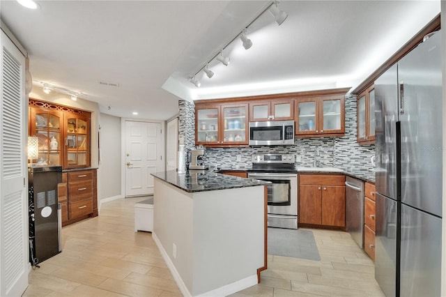 kitchen with stainless steel appliances, sink, tasteful backsplash, dark stone countertops, and track lighting