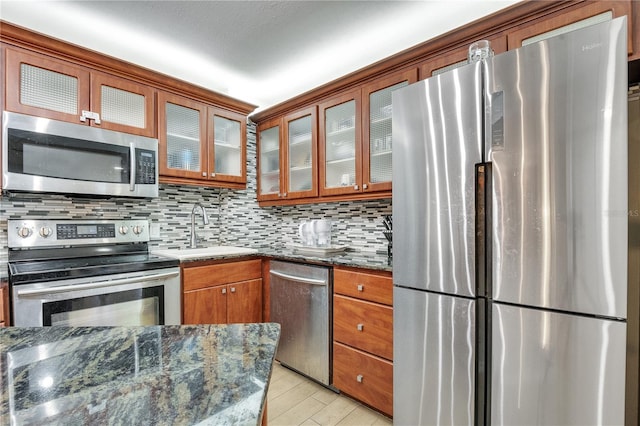 kitchen featuring appliances with stainless steel finishes, tasteful backsplash, dark stone countertops, sink, and light wood-type flooring