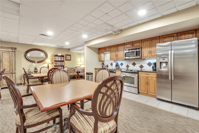 interior space with tasteful backsplash, stainless steel appliances, a paneled ceiling, and light tile floors