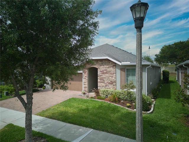 view of front of property with stone siding, roof with shingles, an attached garage, decorative driveway, and a front lawn