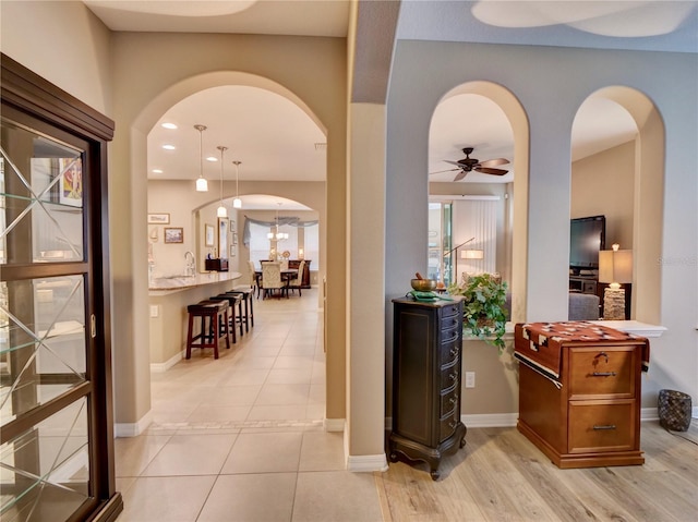 hall with arched walkways, light tile patterned flooring, and baseboards