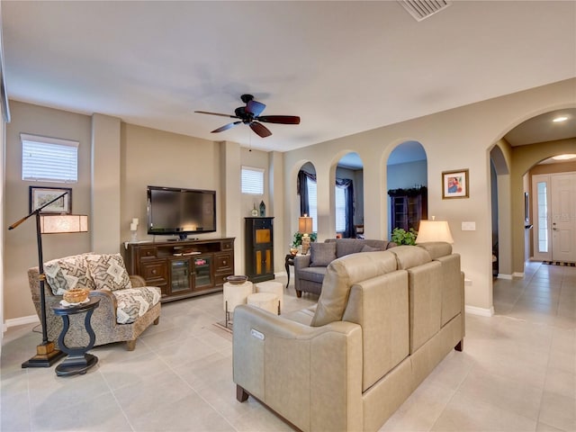 living room with light tile patterned floors, visible vents, arched walkways, a ceiling fan, and baseboards