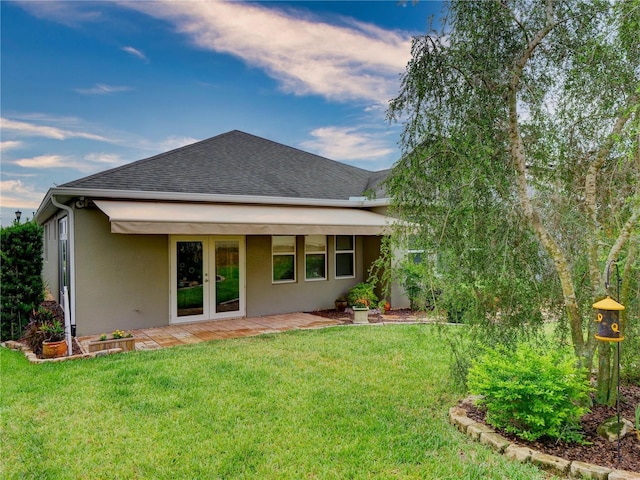 rear view of house featuring a shingled roof, french doors, a lawn, stucco siding, and a patio area