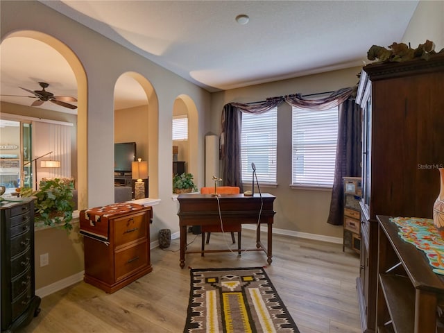 office space with arched walkways, ceiling fan, light wood-style flooring, and baseboards