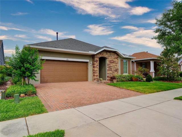 single story home featuring stone siding, stucco siding, an attached garage, decorative driveway, and a front yard