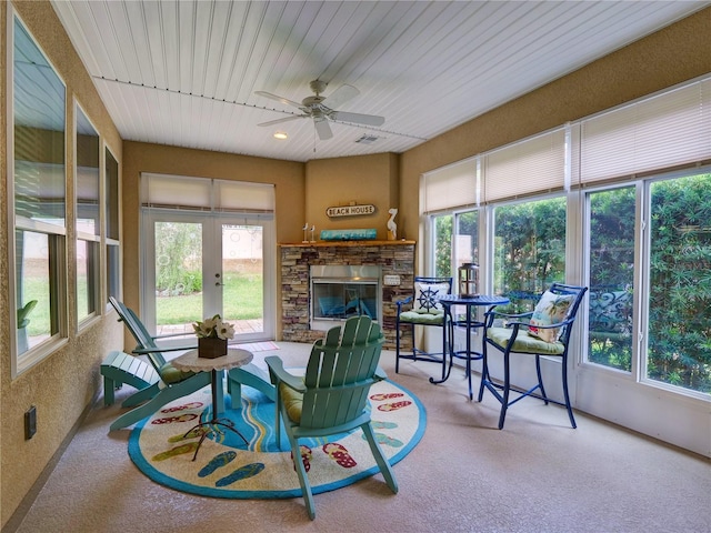 sunroom / solarium with ceiling fan, a stone fireplace, and plenty of natural light