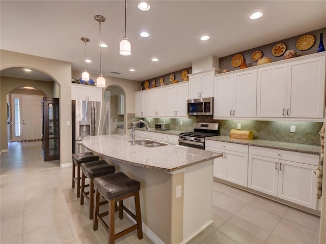 kitchen featuring decorative backsplash, arched walkways, stainless steel appliances, and a sink