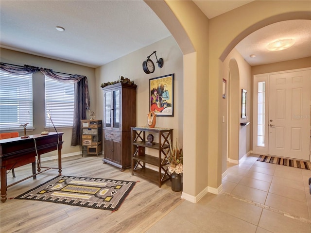 foyer featuring light wood-style floors, arched walkways, and baseboards