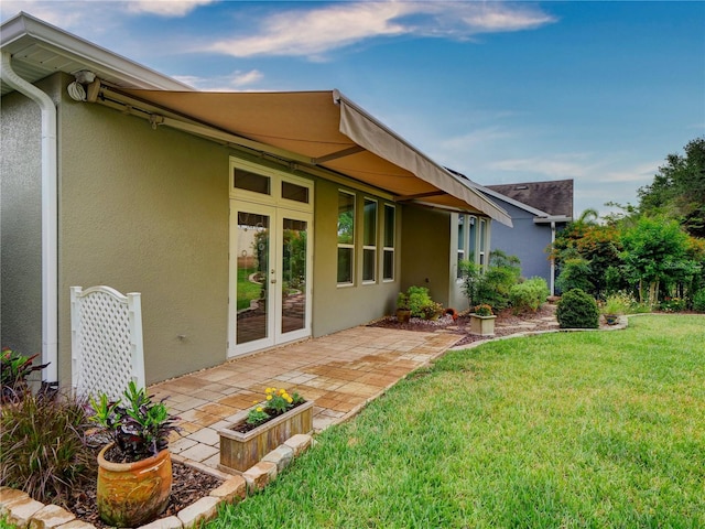 rear view of property featuring a patio, french doors, a lawn, and stucco siding