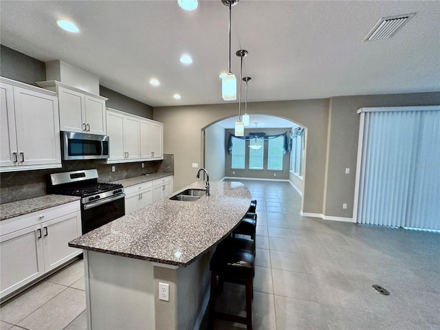 kitchen with visible vents, arched walkways, appliances with stainless steel finishes, a sink, and backsplash