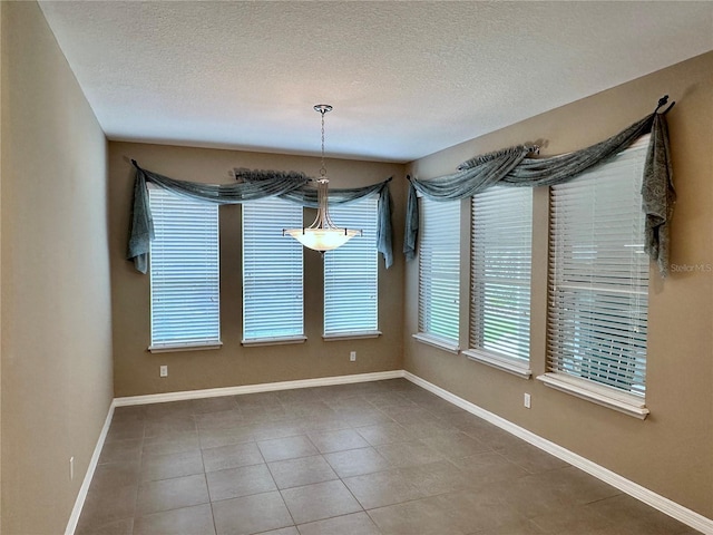 unfurnished dining area with a textured ceiling, tile patterned floors, and baseboards