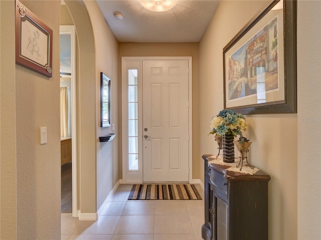 foyer entrance with light tile patterned floors, baseboards, arched walkways, and a textured ceiling