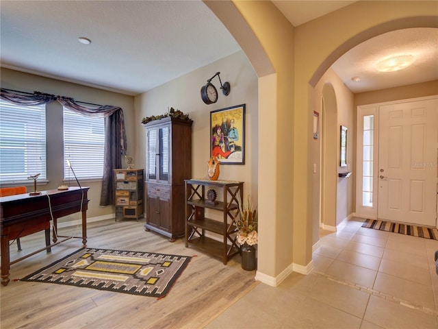 foyer entrance featuring arched walkways, light wood-style flooring, and baseboards