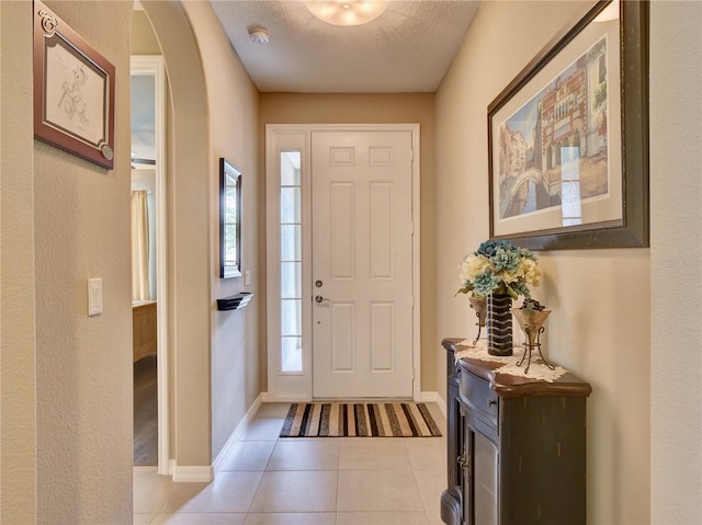 foyer featuring arched walkways, a textured ceiling, baseboards, and light tile patterned floors