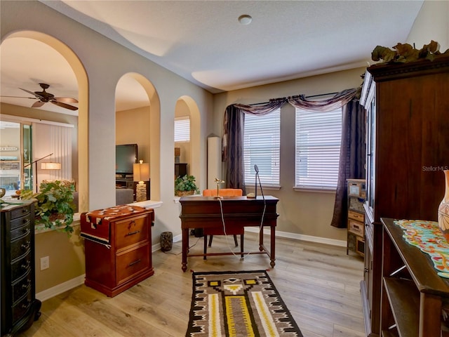 office with ceiling fan, light wood-type flooring, arched walkways, and baseboards