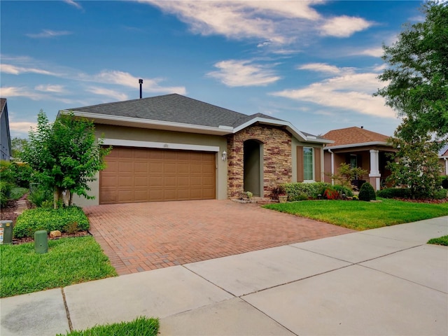 ranch-style house with decorative driveway, stucco siding, an attached garage, a front yard, and stone siding