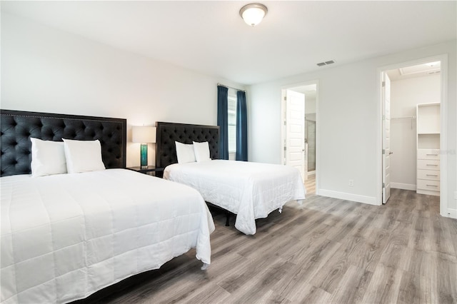 bedroom featuring visible vents, baseboards, ensuite bathroom, a spacious closet, and light wood-style floors