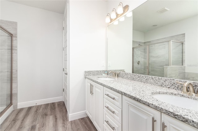 bathroom featuring double vanity, wood finished floors, a stall shower, and a sink