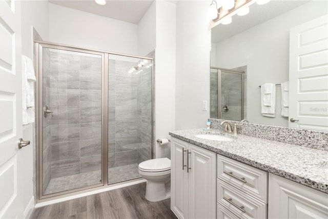 bathroom with a shower with door, wood-type flooring, vanity, and toilet