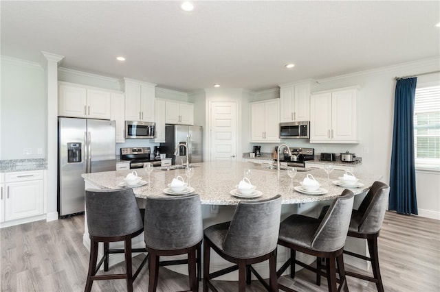 kitchen with appliances with stainless steel finishes, a sink, a large island with sink, and white cabinetry