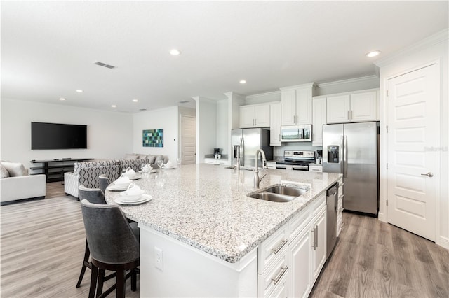 kitchen featuring light hardwood / wood-style flooring, an island with sink, sink, white cabinets, and appliances with stainless steel finishes