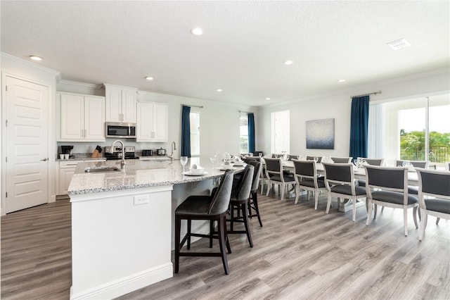 kitchen with a kitchen island with sink, light stone countertops, light wood-type flooring, white cabinets, and sink