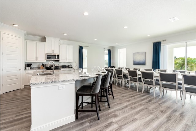 kitchen with white cabinets, a large island, stainless steel microwave, a breakfast bar, and a sink