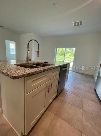 kitchen featuring light stone counters, dishwashing machine, an island with sink, sink, and light tile floors