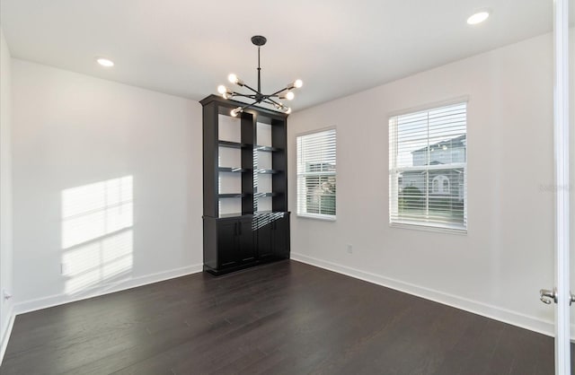 spare room with a notable chandelier and dark hardwood / wood-style flooring