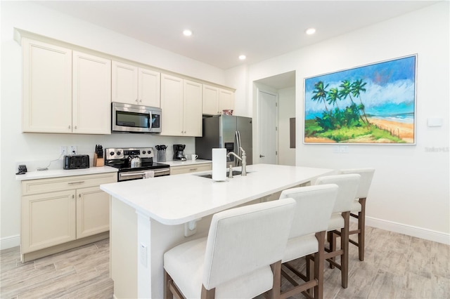 kitchen with stainless steel appliances, light wood-type flooring, sink, a breakfast bar, and a kitchen island with sink