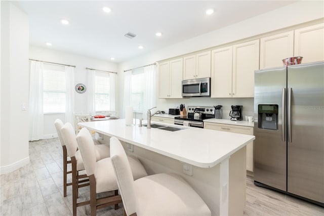 kitchen featuring light hardwood / wood-style flooring, stainless steel appliances, sink, a breakfast bar, and a kitchen island with sink