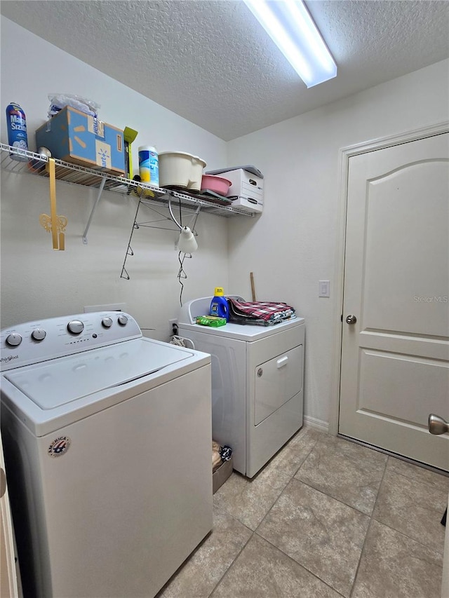 clothes washing area with a textured ceiling, washer and clothes dryer, and light tile flooring