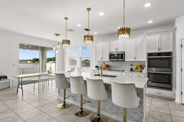 kitchen with hanging light fixtures, stainless steel appliances, white cabinets, a kitchen island with sink, and tasteful backsplash