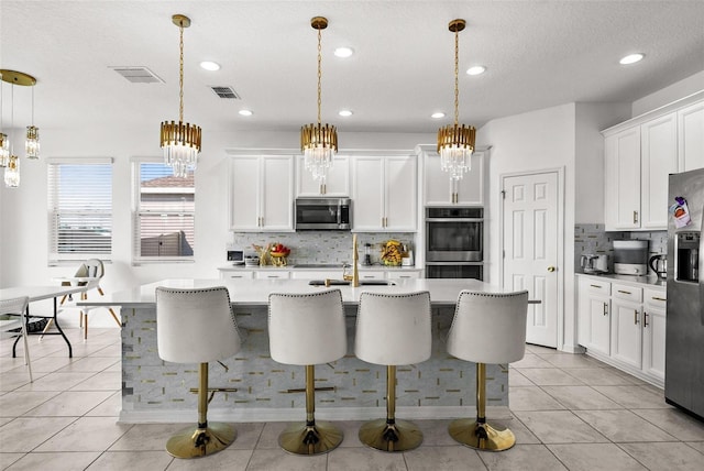 kitchen with decorative light fixtures, white cabinets, light tile floors, and stainless steel appliances