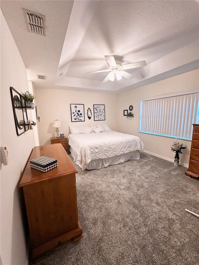 carpeted bedroom featuring a textured ceiling, ceiling fan, and a raised ceiling