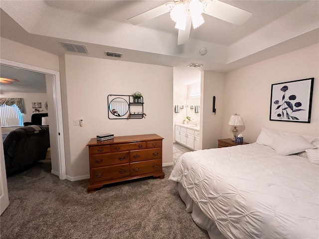 carpeted bedroom featuring ceiling fan, a tray ceiling, and ensuite bath