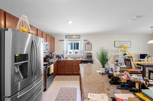 kitchen with decorative light fixtures, stainless steel appliances, light tile floors, sink, and a textured ceiling