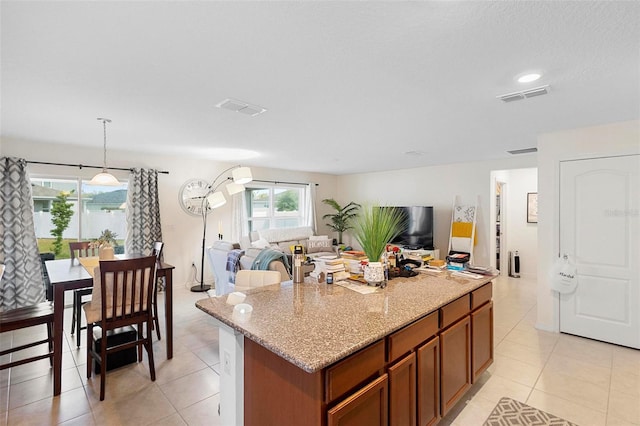 kitchen featuring a center island, light stone counters, light tile flooring, and pendant lighting