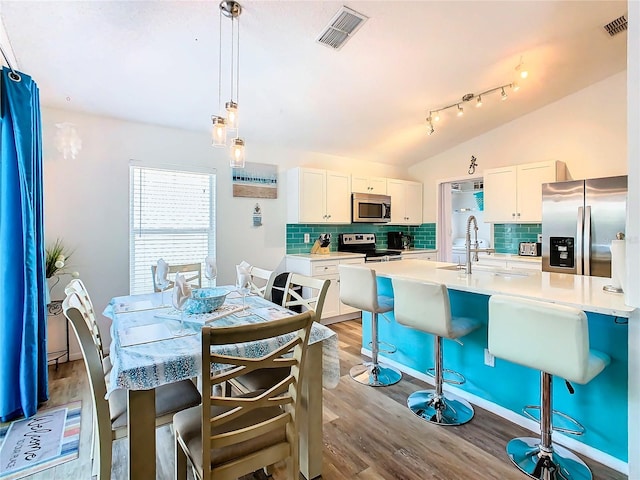 dining area with vaulted ceiling, sink, light hardwood / wood-style flooring, and rail lighting