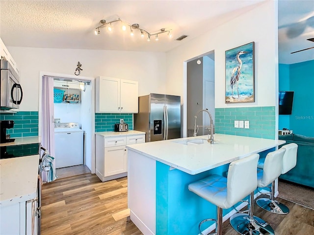 kitchen with washer / dryer, vaulted ceiling, light hardwood / wood-style flooring, stainless steel appliances, and sink