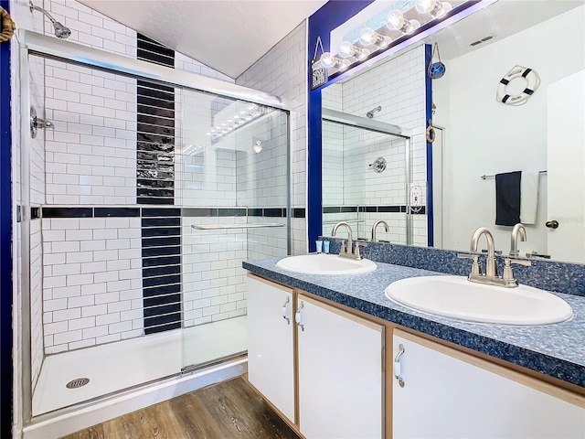 bathroom featuring lofted ceiling, a shower with shower door, hardwood / wood-style floors, vanity with extensive cabinet space, and dual sinks