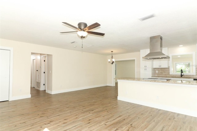 unfurnished living room with ceiling fan with notable chandelier and light hardwood / wood-style flooring